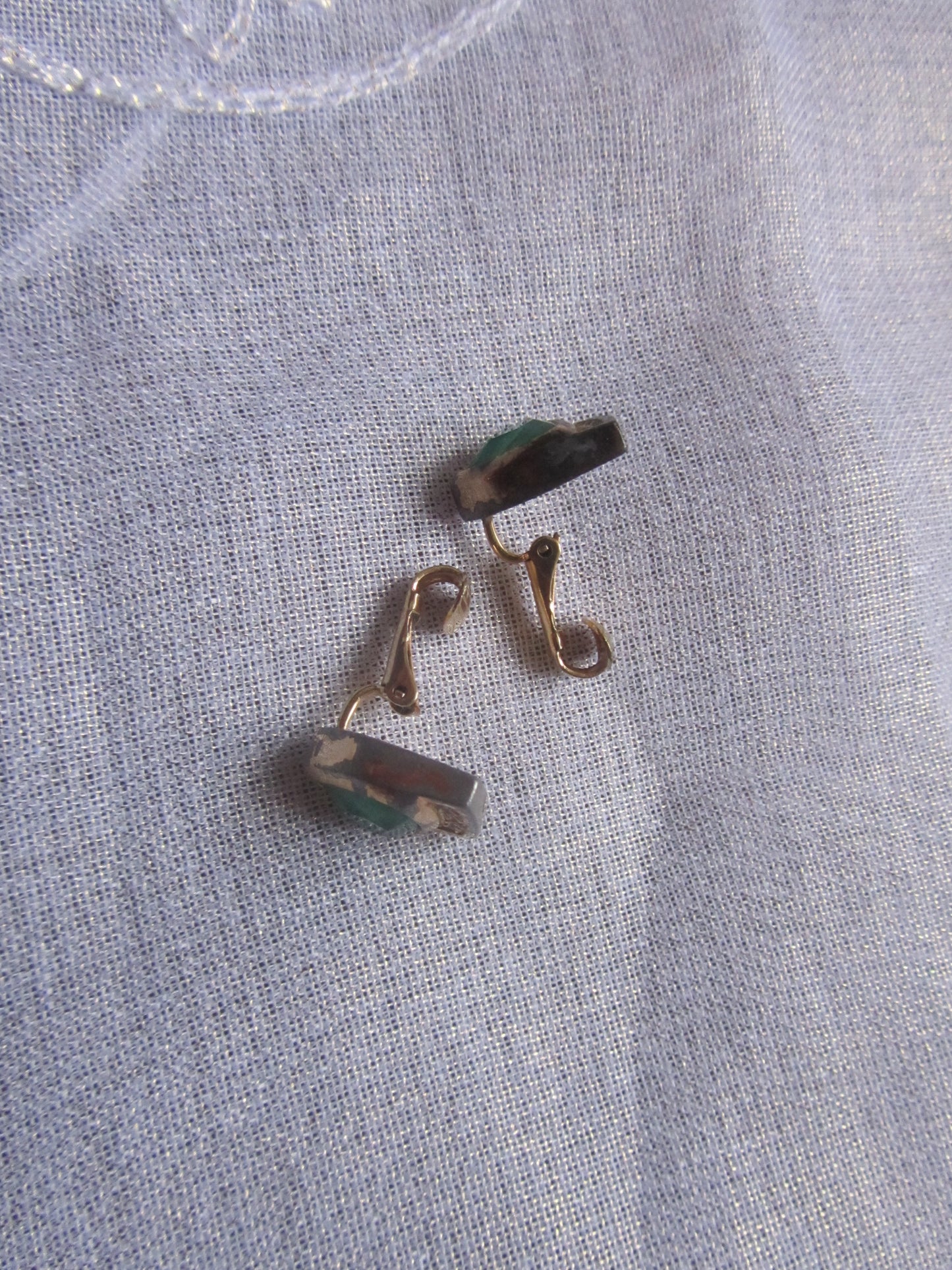 Gold earrings on a textured gray fabric background
