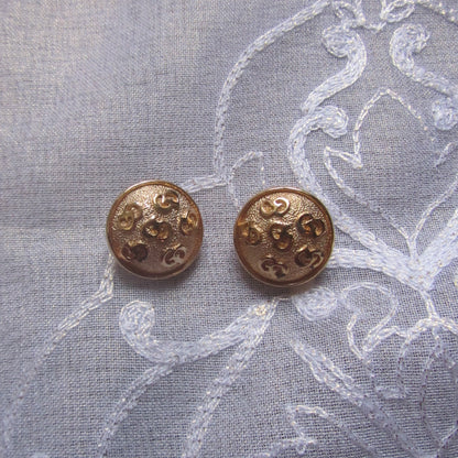 Two bronze earrings on a textured fabric background