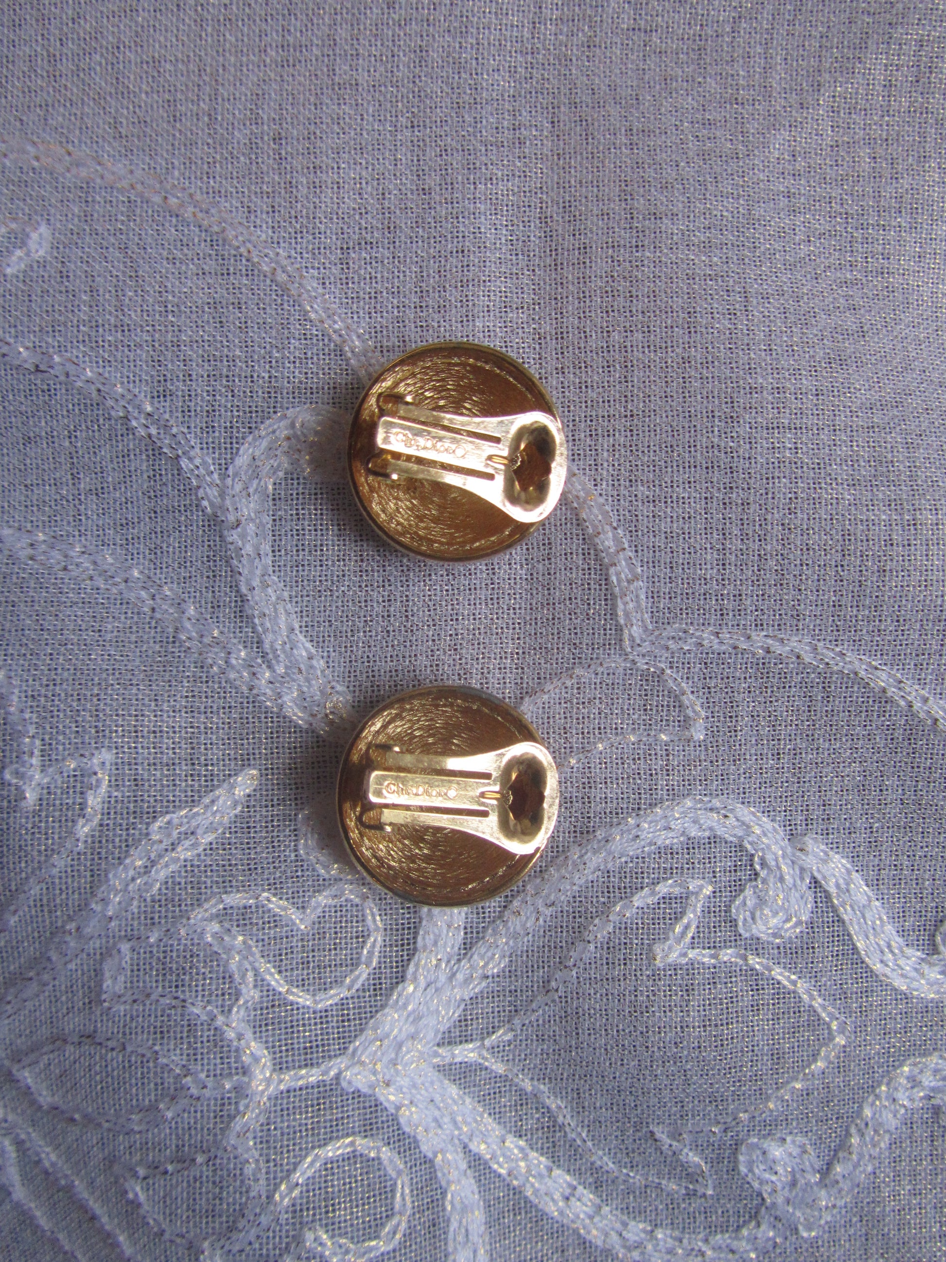 Two gold earrings on a textured gray fabric background