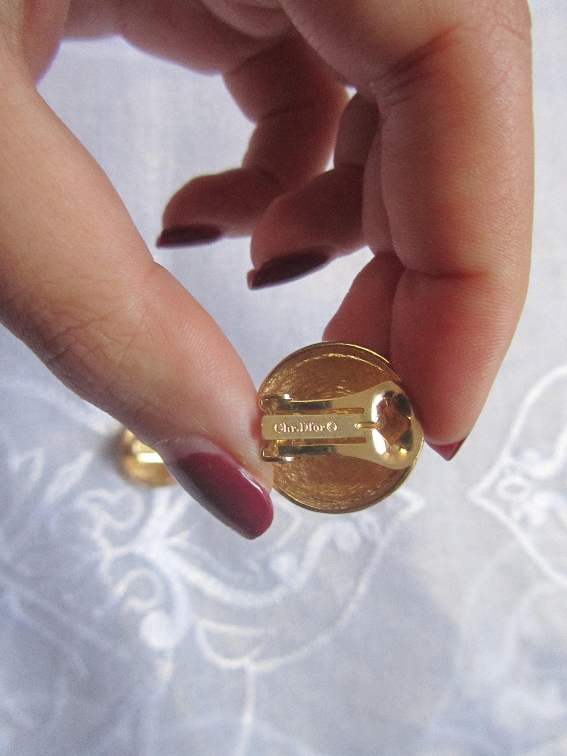 Gold earring held between fingers with a blurred background