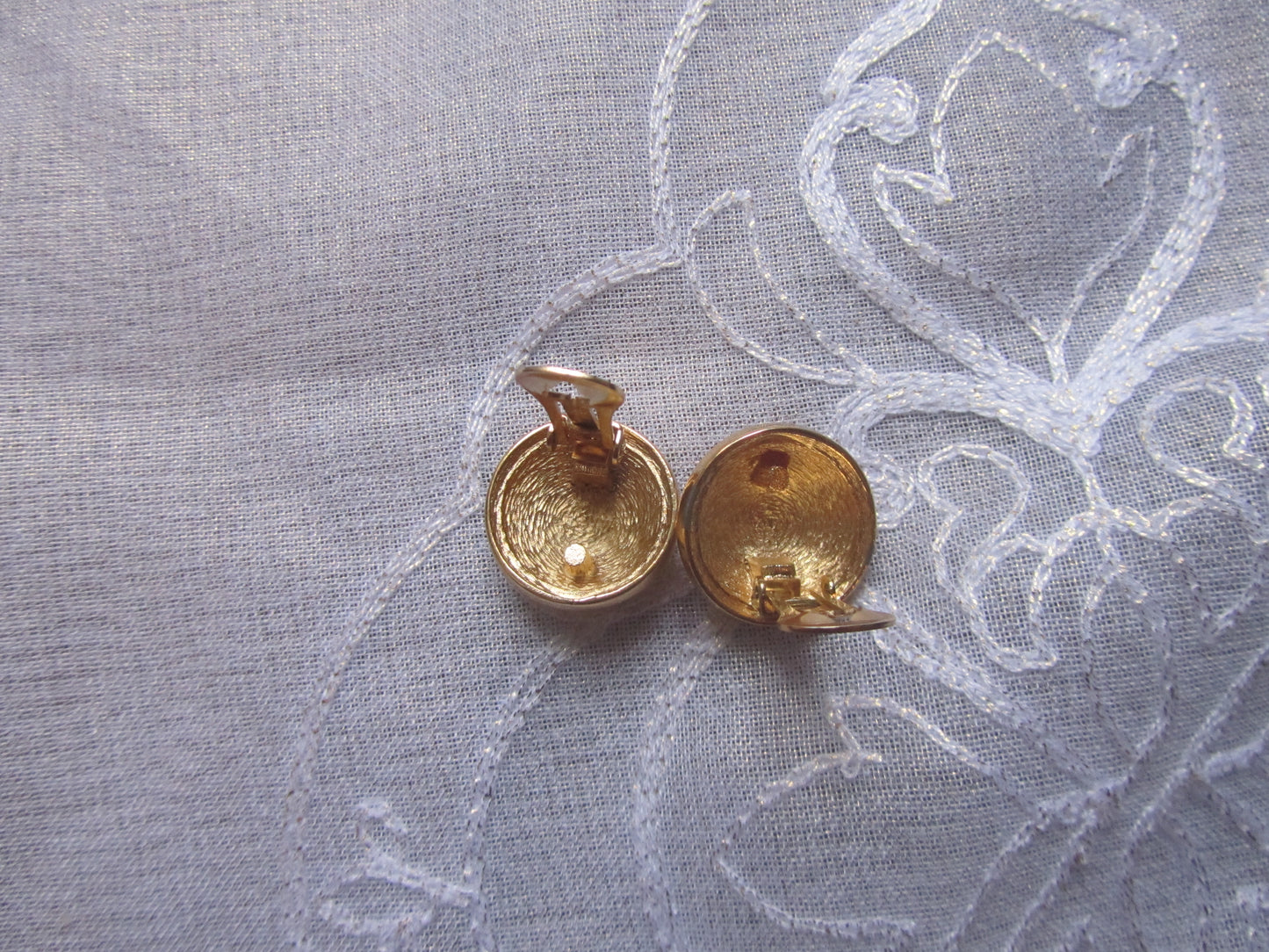 Two bronze earrings on a textured fabric background