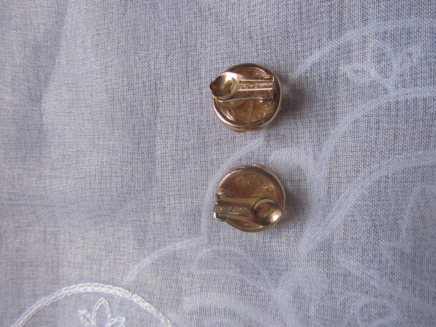 Two gold earrings on a light gray fabric background