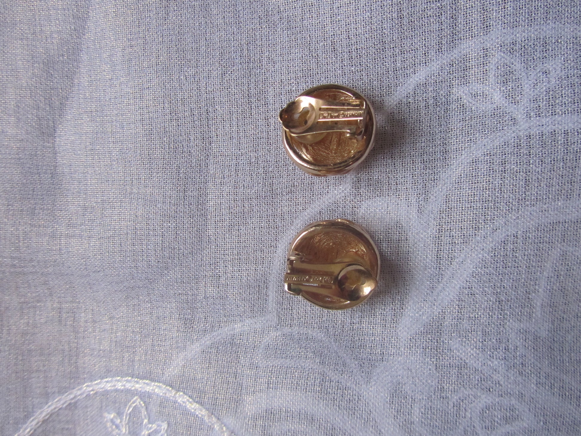 Two gold earrings on a light gray fabric background