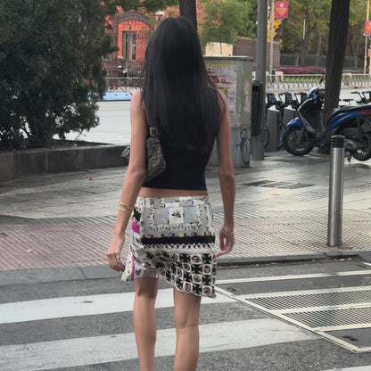 Woman walking on a sidewalk wearing a black top and patterned skirt.