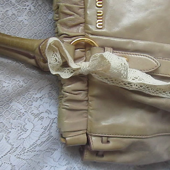 miu miu vintage beige handbag with lace ribbons on a white textured surface