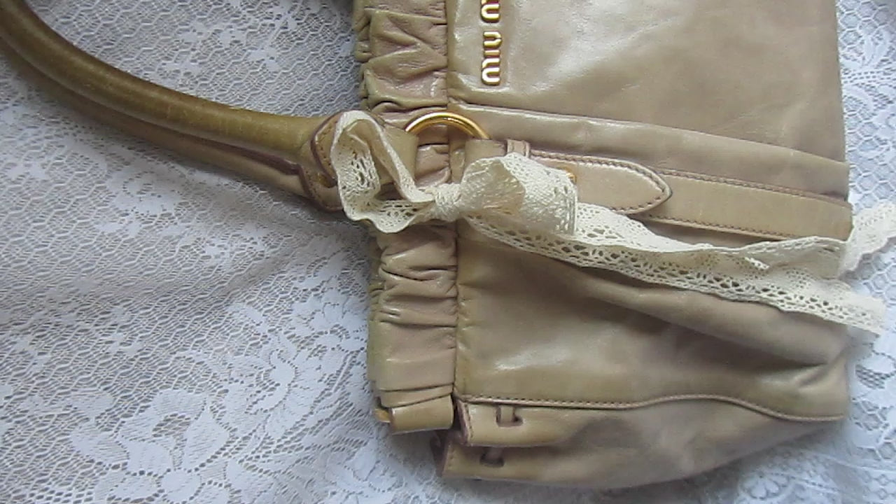 miu miu vintage beige handbag with lace ribbons on a white textured surface